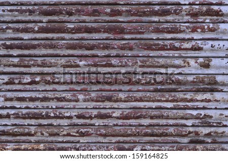 Close up of red, brown rusted metal roll up door in old, distressed condition and look with some coated paint is peeling off