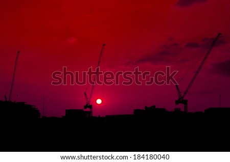 Silhouette construction cranes on top of under construction site at sunset
