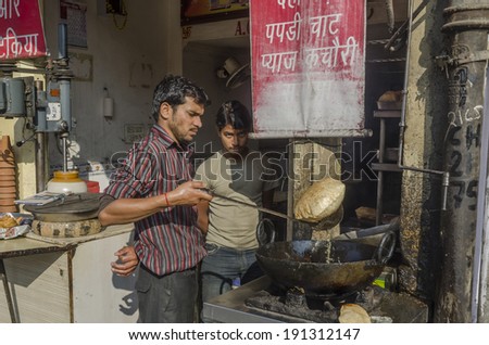 Jaipur, India - March 1, 2014 - Street food vendor preparing and selling meal and snack  for customers at local market during daytime