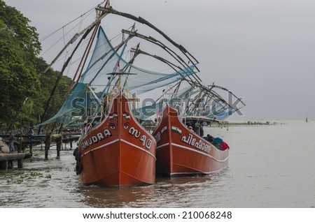 Kerala, India - August 4, 2014 - Fishermen working in red fishing boast floating in the ocean with fishing traps at the background under cloudy sky of monsoon season