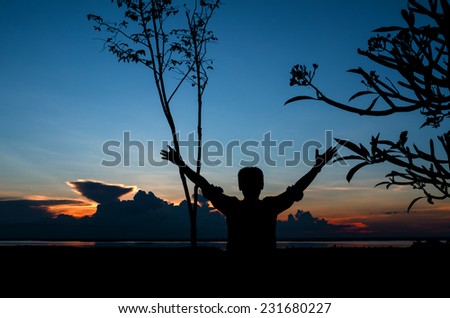 Silhouette man raising hands with cheers against dramatic sky of sunset scene with clouds and river
