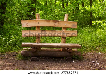 Wooden bench with backrest in a forest. Spring season. Green vegetation around.