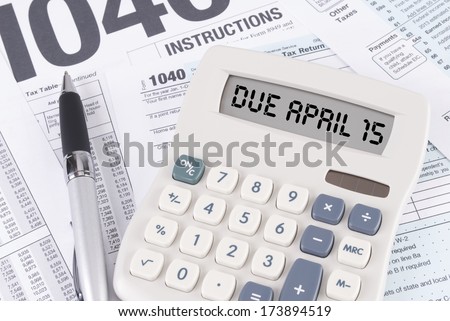 Tax Forms and Pen with a Calculator that spells out DUE APRIL 15 on the display