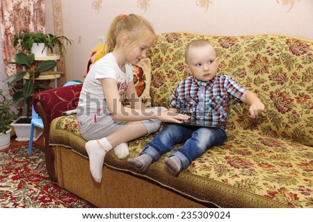 the brother with the sister sit on a sofa and work with the tablet computer