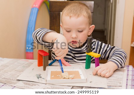 the little boy sits at a table and is engaged in a molding from plasticine