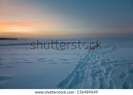 Footprints and tracks in snow on a lake at sunrise