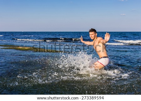 Naked young man jumping for joy from see water (water splash in focus)