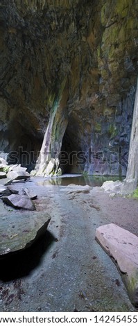 Cathedral Quarry in Cumbria, UK. The main hall with the column and the pond lit by natural light trough a window. A vertical panorama.