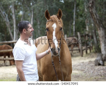 Handsome man looks at dun quarter horse in bridle