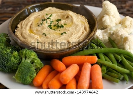 Homemade hummus, drizzled with olive oil, with vegetables including carrots, broccoli, cauliflower, and beans