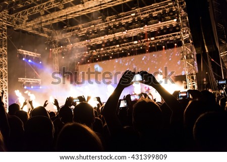 Rock concert, silhouettes of happy people raising up hands in front of bright stage lights