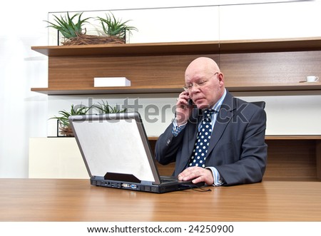 A company executive sitting at his desk, talking on his mobile telephone