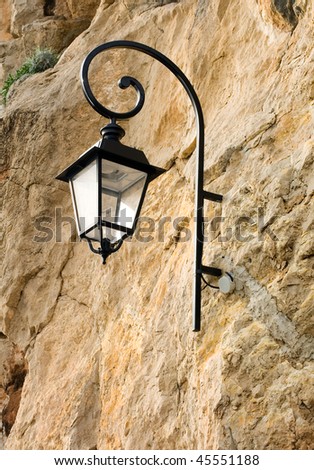 A street lamp attached to a rock wall adjacent to a walkway in Monte Carlo, Monaco
