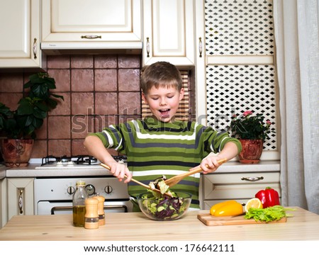 Little boy preparing a salad in the kitchen. Smiling boy mixing vegetable salad.