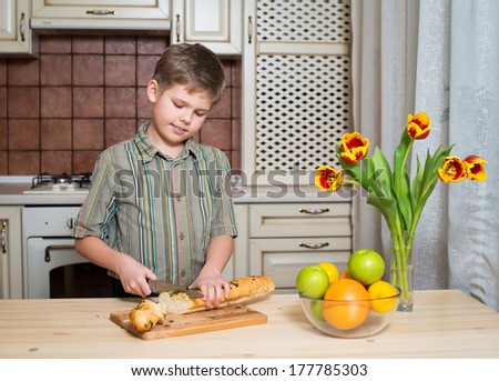 Smiling boy cutting a slice of long loaf.