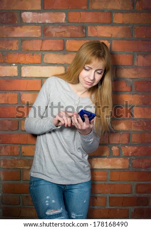 Beautiful woman using high tech smartphone against brick wall.