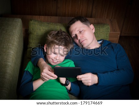 Father and son lying on sofa with an e-reader. Bedtime story.
