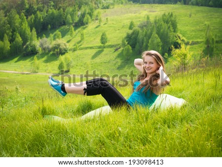 Sit-ups - fitness girl training sit up outside in grass in summer. Happy fit woman doing side crunches with elevated legs while smiling happy.
