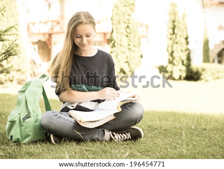 Beautiful school or college girl sitting on the grass with book and bag studying in a park. Retro styled.