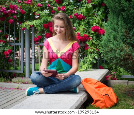 Young pretty teenage girl student using digital tablet in the park near a campus.