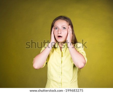 Close-up portrait of surprised beautiful girl holding her head in amazement and open-mouthed. Over yellow background. Young woman shocked and frightened.