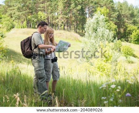 Happy hiking couple smiling during hike in forest. Couple tourists with map in the park. Adventure. Tourists examining map while standing in nature