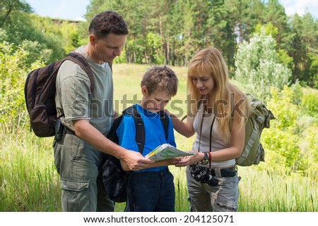 Hiking family with backpacks in the forest discussing the route. Happy couple with son looking at the map.