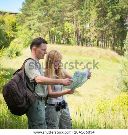 Happy hiking couple smiling during hike in forest. Young couple tourists with map in the park. Adventure. Tourists examining map while standing in nature