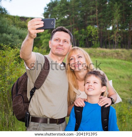 Happy family taking selfie photo with smart phone hiking in the forest. Father, mother and son hiker with backpacks taking self picture photo with smart phone camera. Healthy lifestyle.