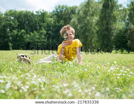 Happy boy enjoying sunny summer or autumn day in nature on green grass. Kid with magnifying glass outdoors.