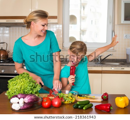 Young beautiful woman and girl making fresh vegetable salad. Healthy domestic food concept. Smiling mother and funny playful daughter cooking together, help children to parents.