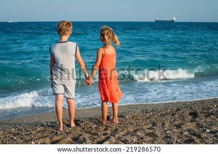 Photo of happy children watching the sea. Young friends portrait at the beach looking at the ship.