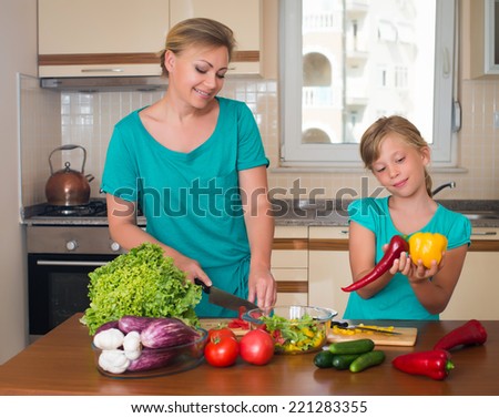 Young woman and girl making fresh vegetable salad. Healthy domestic food concept. Smiling mother and funny playful daughter cooking together, help children to parents.
