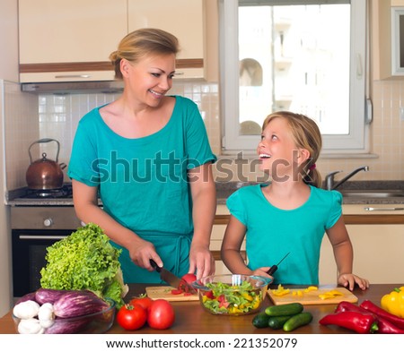 Young woman and girl making fresh vegetable salad. Healthy domestic food concept. Smiling mother and funny playful daughter cooking together, help children to parents.