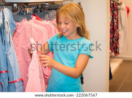 Little girl shopping in clothes store. Child chooses dress at clothes shop.