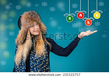 Winter sales concept. Winter woman is pointing showing a word sale on colorful Christmas baubles.