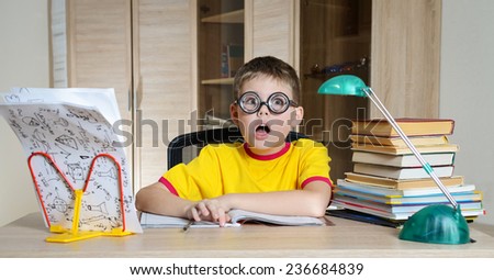 Confused schoolboy in funny glasses screaming near the huge stack of books. Education. Boy Having Problems With His Homework.