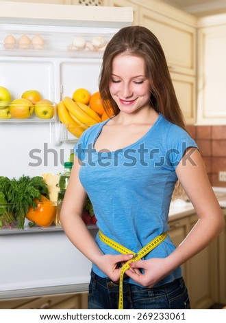 Healthy woman standing near open fridge full of vegetables and fruit, athletic girl with measure tape, organic food concept.