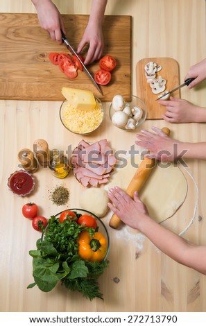 Mother and her children cooking pizza at home. Filling pizza with ingredients. Top view. Overhead view.