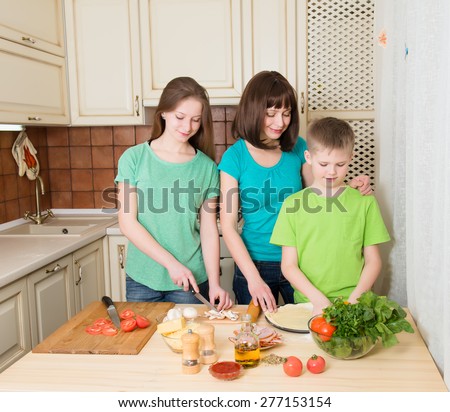 Teenager boy and girl with their mother cooking pizza at home. Portrait of mom with her helping kids making pizza in the kitchen.