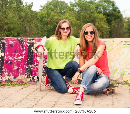 Happy teenagers outdoors. Summer. Girl friends having fun together with skate board. Urban lifestyle.