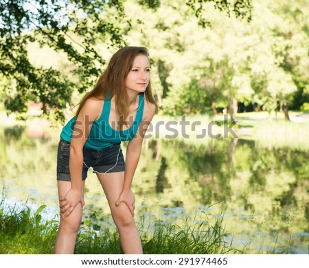 Close-up of runner girl outdoors resting on the bank of the lake or river. Tired but happy beautiful sports fitness model living healthy active lifestyle.