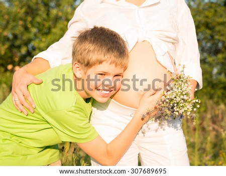 Happy boy holding listens belly of pregnant woman. Mothers day concept.
