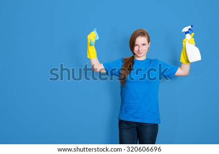 Maid cleaning woman with cleaning spray bottle. Cleaning service. Portrait of beautiful cleaning girl isolated on blue background with copyspace. Mixed race woman.