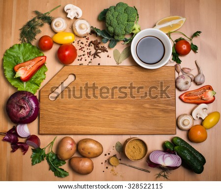 Various vegetables and spices and empty cutting board. Colorful ingredients for cooking on rustic wooden table around empty cutting board with copyspace. Top view. Retro styled.