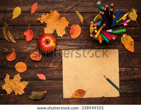 A pencil on the empty vintage paper, an apple and autumn leaves on wooden table. Back to school concept: paper, pencils, apple and colorful leaves. Retro style.
