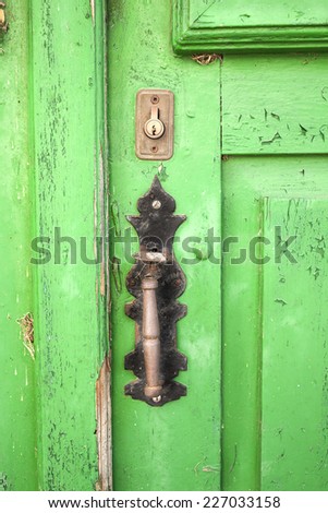 Old wooden door painted green with lock and iron knocker to call.