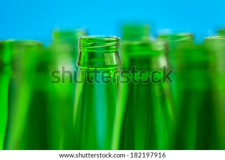 Nine green bottle necks on blue background, in center one bottle in focus.