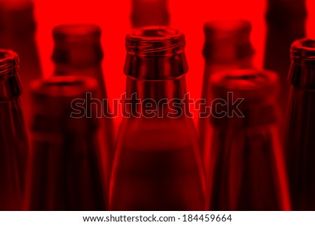 Nine green and one brown bottles shot with red light. Central brown bottle neck in focus.