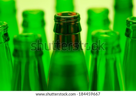 Nine green and one brown bottles shot with green light. Central brown bottle neck in focus.